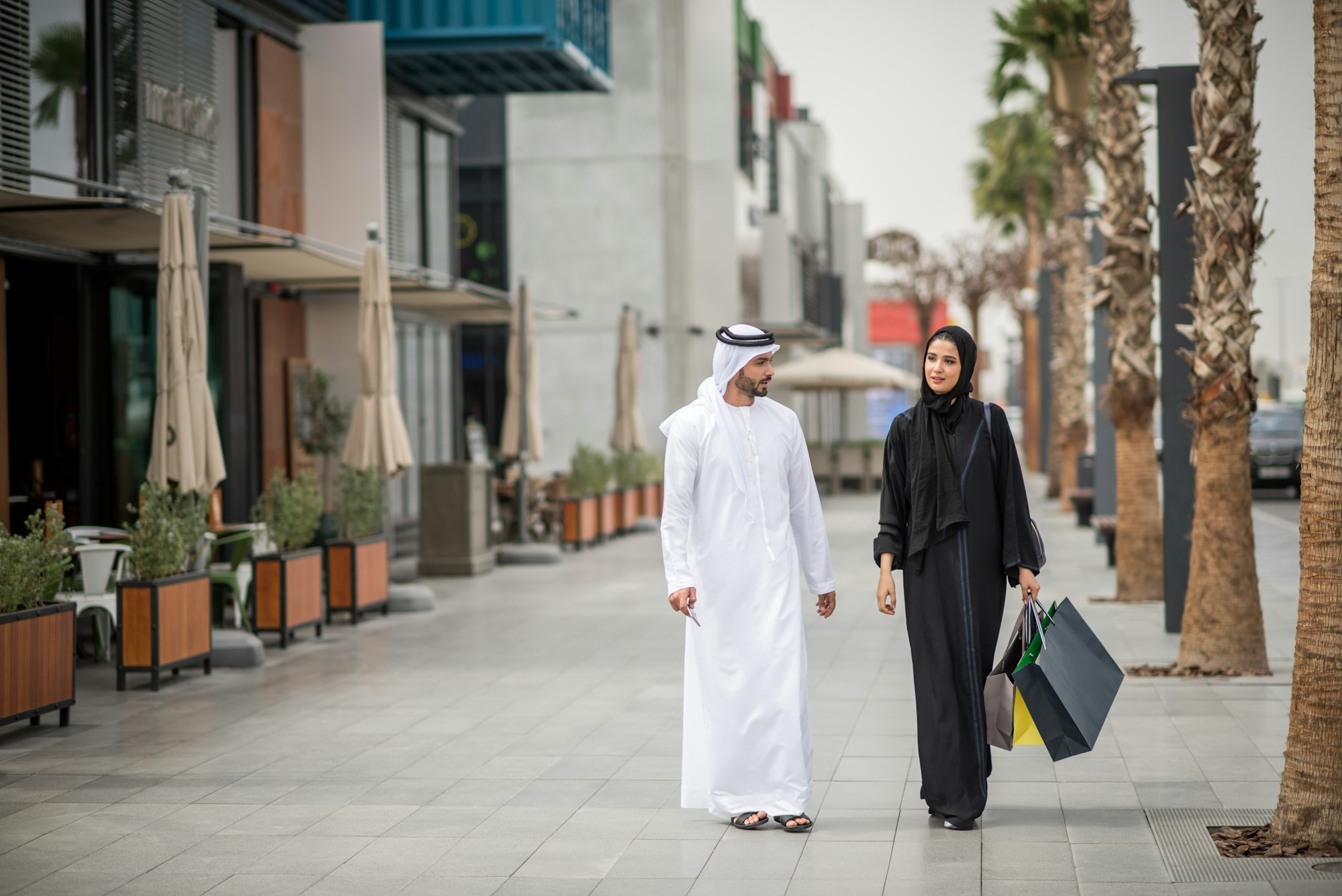 Middle eastern shopping couple wearing traditional clothing carrying shopping bags, Dubai, United